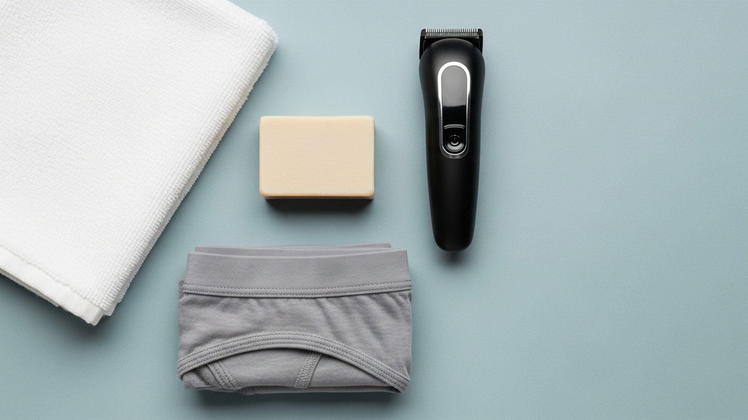 Essentials für die Genitalpflege des Mannes—Handtuch, milde Seife, Trimmer und Baumwollunterwäsche in Pastelltönen
