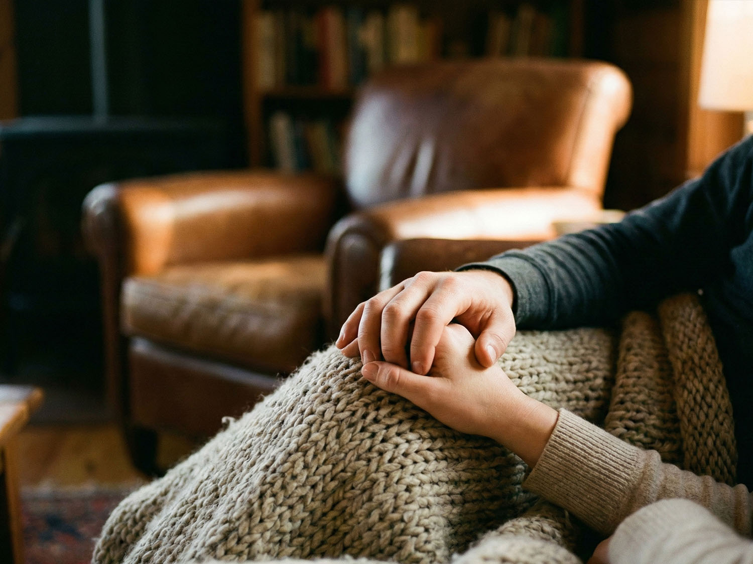 A close-up of a man’s hand gently resting over a woman’s hand on a textured wool blanket.