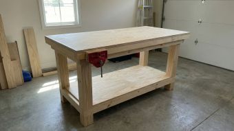 A completed heavy-duty wooden workbench with a double-layered plywood top and a red metal vise in a garage workshop.