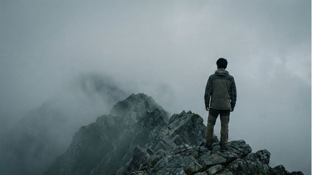 霧のかかった険しい山の尾根に一人立ち、医療への不安を避けている男性。