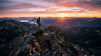 A man standing on a rocky mountain peak overlooking a vast valley at sunrise.