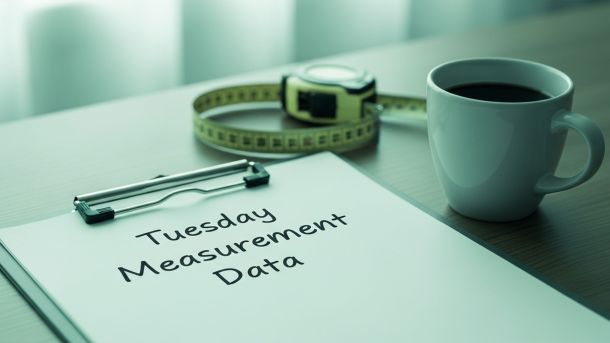 Montaje científico simulado con portapapeles etiquetado como “Datos de medición del martes”, cinta métrica y calendario con el martes rodeado.