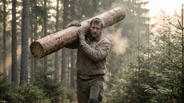 Ein Mann zeigt funktionale Stärke, indem er eine schwere Last in freier Natur trägt.