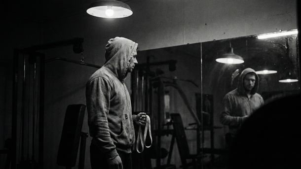 Um homem examinando o seu reflexo, simbolizando a pressão das estatísticas físicas masculinas.
