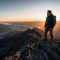 日の出の中、広い谷を見渡す岩山の頂上に立つ男性。
