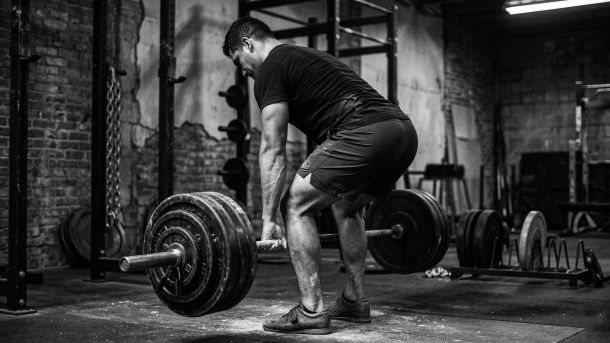 Hombre realizando un levantamiento de peso muerto con barra pesada con soporte corporal completo, lo que representa la activación del suelo pélvico y la estabilidad del tronco en atletas masculinos.