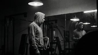 鏡の中の自分を見つめる男性。男性の身体統計によるプレッシャーを象徴している。