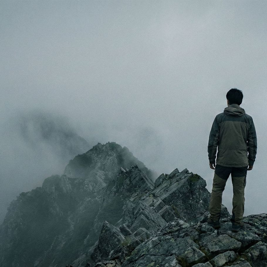 霧のかかった険しい山の尾根に一人立ち、医療への不安を避けている男性。