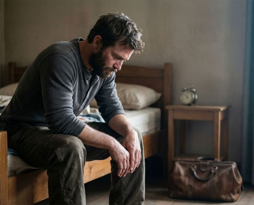Man sitting on edge of bed in early morning light, reflecting the weight of sleep deprivation and stress on male health
