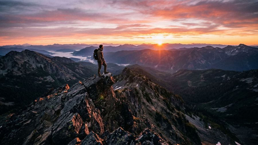 Un homme debout sur un sommet rocheux surplombant une vaste vallée au lever du soleil.