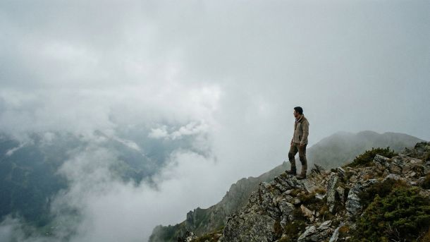 Um homem parado sozinho em uma crista de montanha nebulosa e escarpada, evitando preocupações médicas.