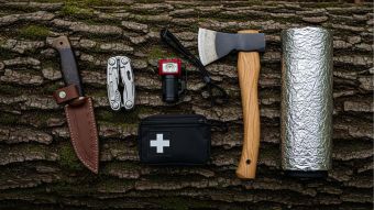 Flachlage von wichtigsten Überlebenswerkzeugen auf Segeltuch: Messer, Multitool, Feuerstahl, Stirnlampe, Wasserfilter, Erste-Hilfe, Paracord, Akkupack, Klappsäge, Rettungsdecke.